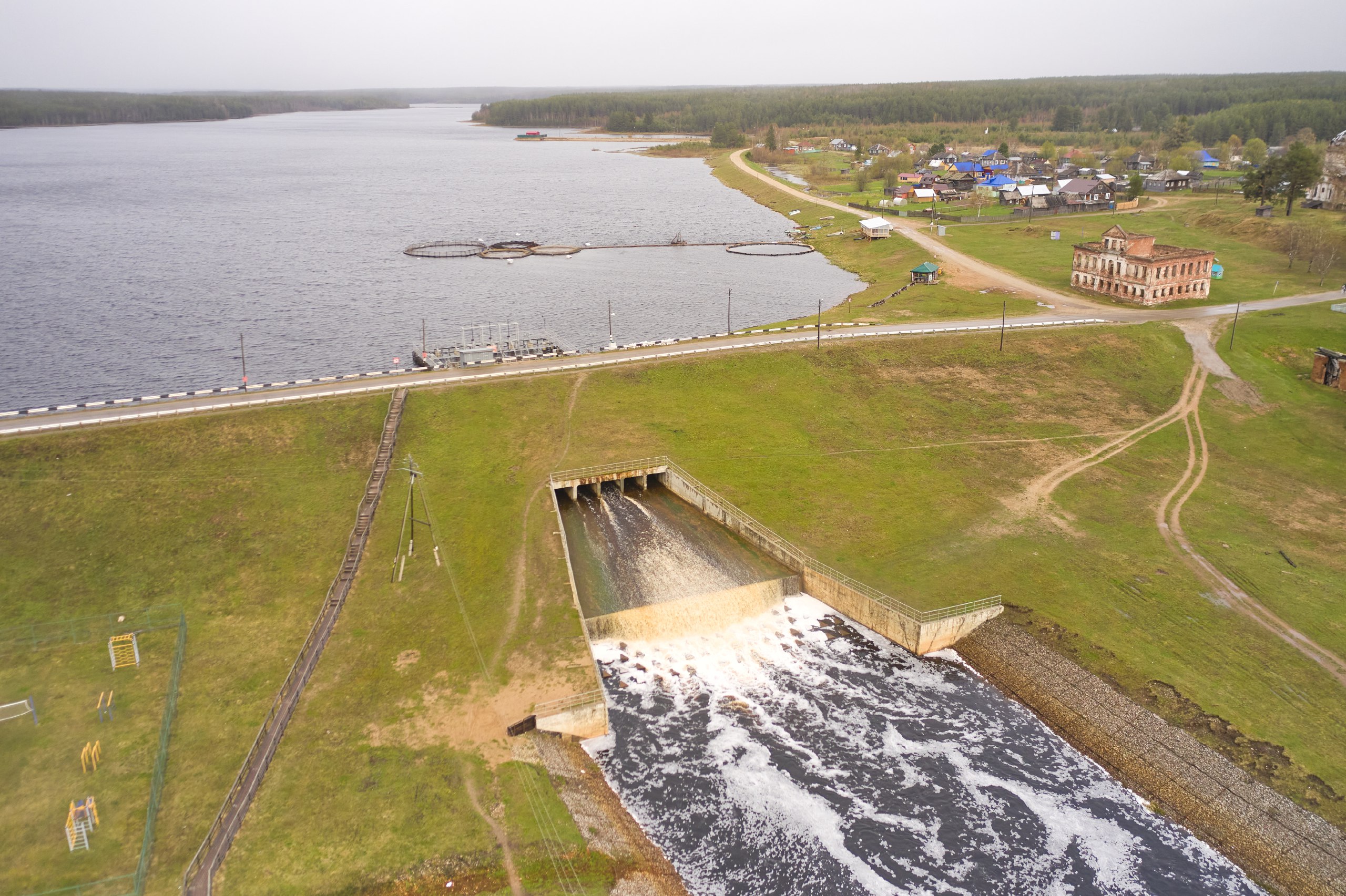 Вид сверху на плотину с водосбросом, прибрежную зону и здание в поселке Кажым во время полевой съёмки